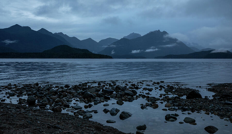 Moody mountain reflections and rocky shoreline at Kennedy Lake on Vancouver Island British Columbia