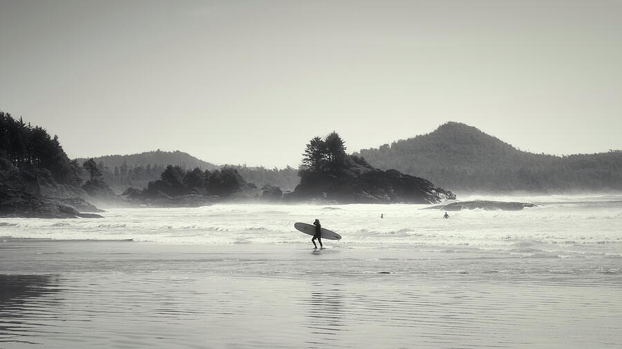 Black and white photograph of a surfer walking from the water at Long Beach near Tofino Vancouver Island