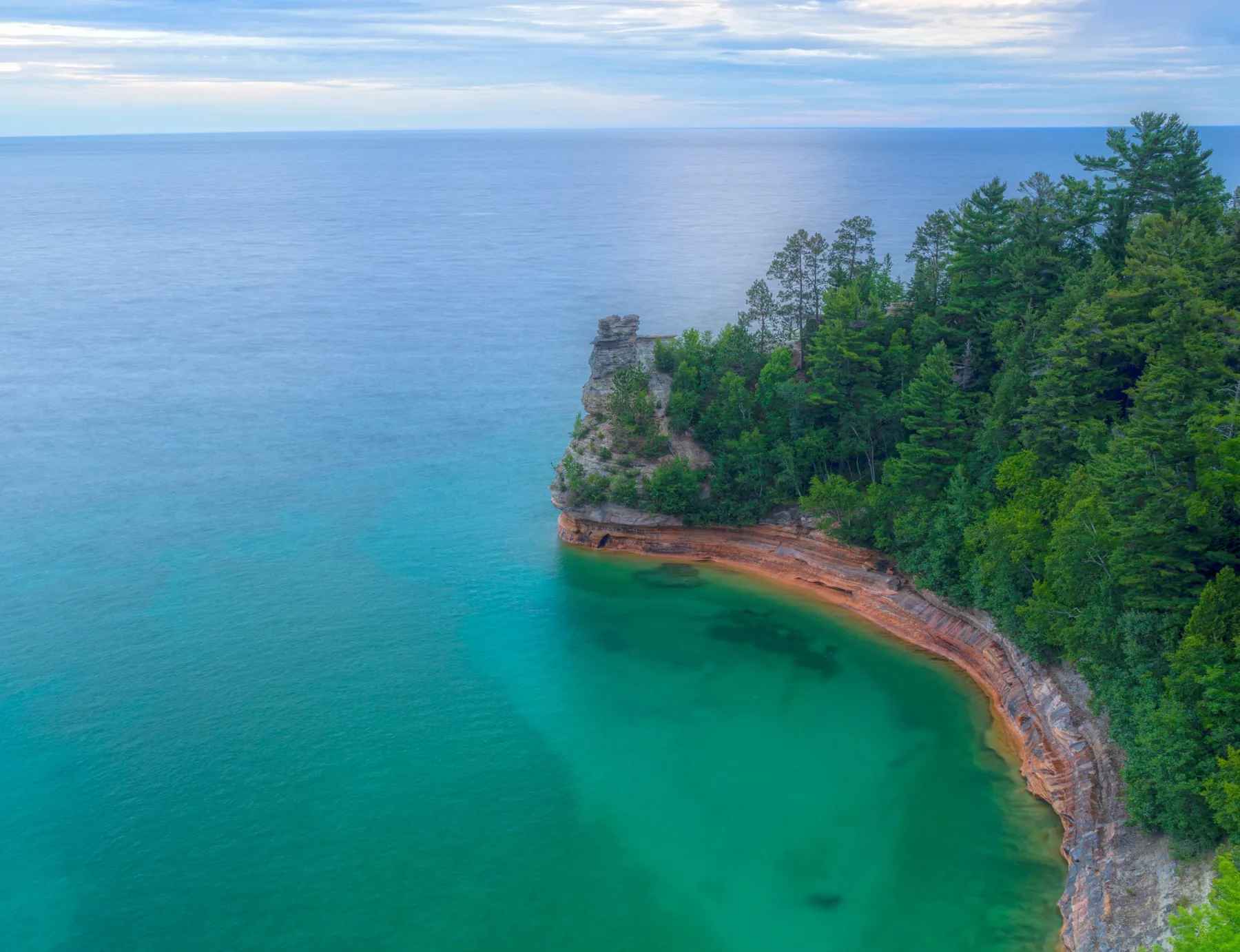Blue-green Lake Superior water along a forested cliff